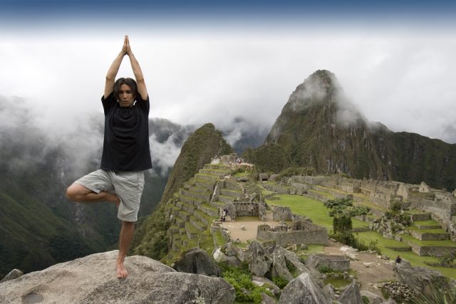 A male tourist does the tree yoga pose at the ancient historical Inca city of Machu Picchu in Peru. Wide angle view.