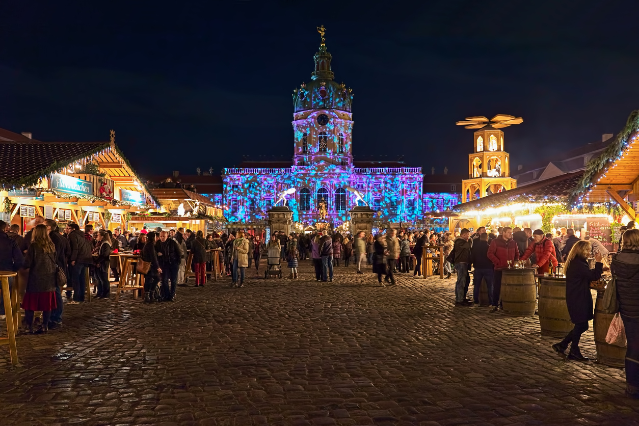 Berlin, Germany - December 3, 2018: Christmas Market in front of the famous Charlottenburg Palace in night. Unknown people walk around the market stalls and consume food and drinks. Facade of the Palace is illuminated with Christmas lights show.