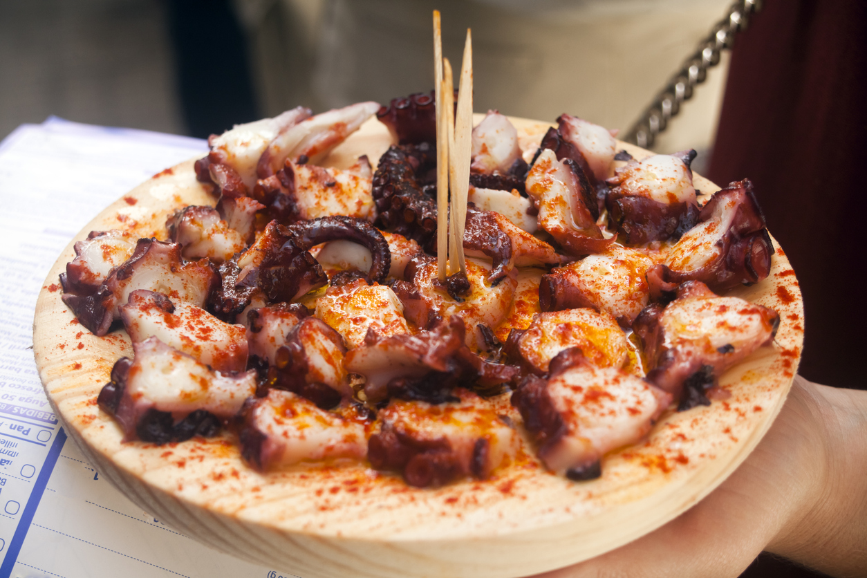 Octopus 'pulpo a feira' style, traditional dish in Galicia, Spain. Slices of boiled octopus served with salt,paprika and olive oil on a wooden plate.